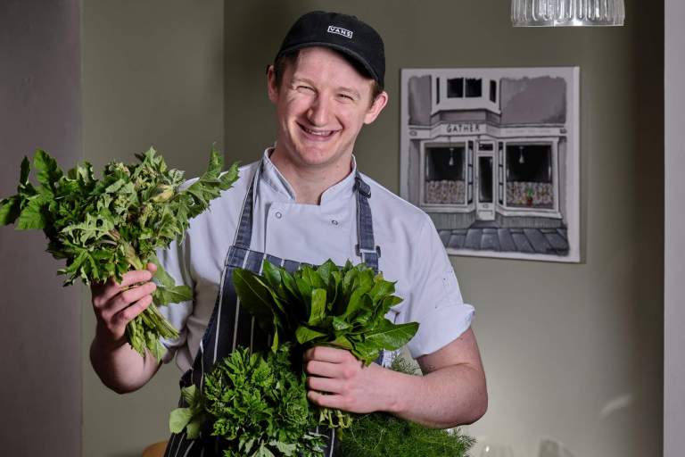 Harrison Brockington holding locally sourced produce in his restaurant, Gather