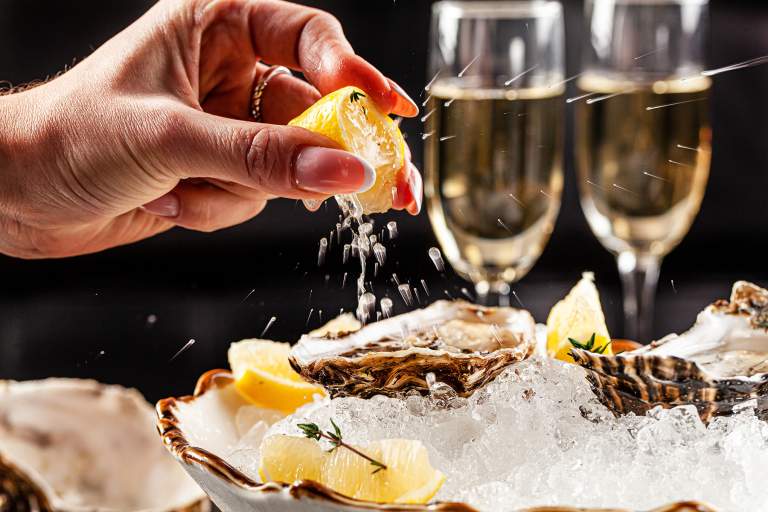 Squeezing lemon onto seafood with two glasses of champagne in the background