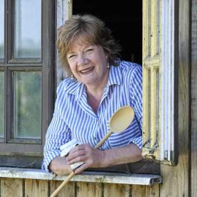 Ann Stallard, Waterhouse Fayre. Smiling ,looking out of window holding a wooden spoon